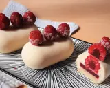 Entremets vanille-framboise sur assiette rayée, décorés de framboises fraîches.