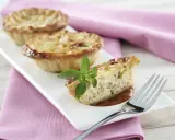 Une délicieuse petite quiche lorraine, garnie d'une touche de basilic frais, attend d'être dégustée sur une assiette blanche.