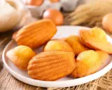 Des madeleines dorées, parfaites pour une recette gâteau madeleine meilleur pâtissier. Des œufs et de la farine en arrière-plan.
