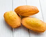Trois madeleines dorées, tout juste sorties du four, sur une planche en bois. La cuisson madeleine est réussie, leur texture est parfaite.