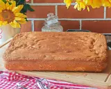 Une génoise rectangulaire dorée, parfaite pour 15 personnes, attend d'être garnie. Des fleurs jaunes et un fond de briques rouges créent une ambiance chaleureuse.