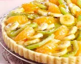 Tarte aux fruits frais sur une base de crème pâtissière. Des rondelles de banane, de kiwi et des quartiers d'orange sont disposés sur le fond de tarte.