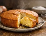 Un délicieux gâteau fait maison, probablement avec 4 œufs, dégage de la vapeur. Une part est coupée et prête à être dégustée.