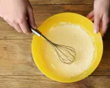 Mains préparant la pâte à crêpes dans un bol jaune. La pâte est prête pour son temps de repos.