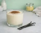 Un verre de crémeux vanille Michalak, saupoudré de cacao, avec des gousses de vanille.