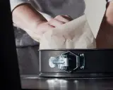 Mains expertes s'affairent à chemiser un moule avec du papier sulfurisé, préparant ainsi le terrain pour une future création culinaire.