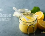 Une recette de crème au citron rapide, prête à être dégustée. Un pot en verre rempli de cette crème onctueuse, avec des citrons frais et des feuilles vertes.