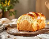 Pain brioché doré, résultat d'une fabrication de levure de boulanger réussie. Farine, fouet et beurre à proximité.