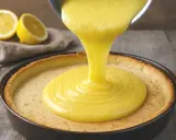Une crème aux citrons onctueuse est versée dans une tarte. Des citrons coupés en deux sont visibles en arrière-plan.