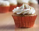 Un cupcake orné d'une généreuse ganache chocolat blanc, parsemé de perles rosées, dans un élégant caissette orange.