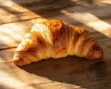 Un délicieux croissant maison, doré et feuilleté, repose sur une table en bois baignée de soleil.