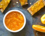 Confiture d'écorce d'orange brillante dans un bol blanc, servie sur des toasts avec des tranches d'orange fraîche.
