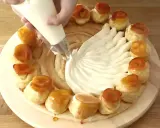 Une main garnit une couronne de choux avec de la crème chiboust, créant un dessert spectaculaire.