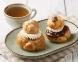Deux religieuses au café, garnies de crème et nappées de chocolat ou de caramel, accompagnées d'une tasse de thé.
