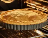 Tarte en cuisson à blanc dans son moule. La pâte brisée est dorée et gonflée, prête à être garnie.