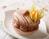 Un délicieux macaron chocolat au lait, garni de crème onctueuse et décoré d'une physalis orangée.