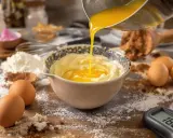 Préparation d'une pâte à bombe : du beurre fondu est versé dans un bol de crème, entouré d'œufs, de farine et de cacao.