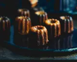 Plusieurs cannelés dorés, parfaits pour la conservation, sont disposés sur une assiette sombre.