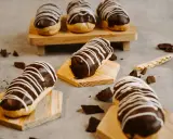 Éclairs gourmands avec un glaçage éclair chocolat brillant, décorés de fines rayures blanches. Des éclats de chocolat parsèment la table.