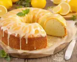 Un cake au citron ultra moelleux, nappé d'un glaçage blanc et jaune, décoré de menthe. Des citrons frais entourent ce délice.