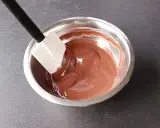Spatule mélangeant une ganache au chocolat noir onctueuse dans un bol en métal.