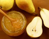 Un pot de confiture de poires maison, avec une cuillère en bois, entouré de poires fraîches coupées et entières sur fond de bois.