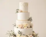 Magnifique gâteau de mariage à quatre étages, décoré de roses pâles, de feuillage et de dentelle dorée. Une inspiration pour toute recette de wedding cake.