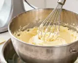 Un batteur électrique fouette une crème au beurre onctueuse dans un bol en acier inoxydable au-dessus d'un bain-marie.