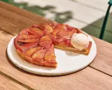 Tarte Tatin caramélisée, une part coupée, servie avec une boule de glace à la vanille. La cuisson parfaite révèle des pommes dorées et une pâte croustillante.