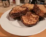 Quatre tranches de pain dur au four, dorées et croustillantes, sur une assiette blanche.