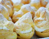 Une assiette de choux à la crème, saupoudrés de sucre glace. Ces petites merveilles de pâtisserie sont prêtes à être dégustées.