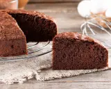 Un délicieux gâteau génoise chocolat, moelleux et aéré, prêt à être dégusté. Des ingrédients frais comme des œufs et du cacao sont visibles en arrière-plan.