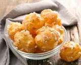 Un bol de chouquettes maison dorées et saupoudrées de sucre perlé, posé sur une table en bois.
