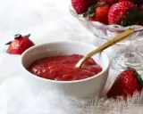 Un bol de compotée de fraise pour gâteau, prêt à être dégusté. Des fraises fraîches sont disposées autour.
