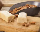 Deux blocs de pâte d'amande et des amandes dans une pelle, prêts pour une recette de pâte d'amande maison.