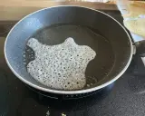 Une pâte fine et aérée cuit dans une poêle, formant une délicate tuile dentelle.