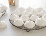 Douces meringues blanches, prêtes pour la cuisson. Elles reposent sur des grilles, évoquant la douceur et la légèreté.