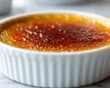 Crème brûlée dans un ramequin blanc, sa croûte caramélisée brillante témoigne d'une cuisson parfaite.