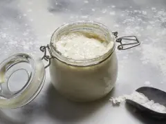 Un bocal ouvert contient une pâte fermentée pétillante, prête pour une recette de pain maison. Une cuillère à farine est à côté.