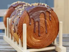 Un délicieux new york roll, feuilleté et garni de chocolat fondant et de noisettes concassées, présenté sur un support en bois.