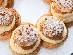Plusieurs Paris-Brest, des pâtisseries rondes à la pâte à choux garnies de crème onctueuse et saupoudrées de sucre glace et d'amandes.