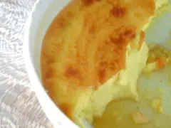Un flan aux œufs à l'ancienne, doré et crémeux, est servi dans un plat blanc. Une part a été retirée, révélant sa texture onctueuse.