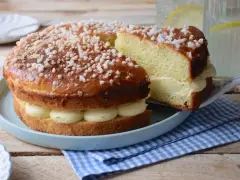Un délicieux gâteau tropézien, garni de crème onctueuse et saupoudré de sucre perlé. Une part est servie sur une pelle à gâteau.