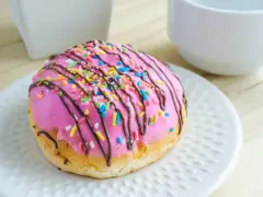 Un délicieux donut avec un glaçage donuts rose vif, garni de vermicelles colorés et d'un filet de chocolat.