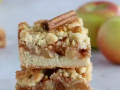 Deux parts de meilleur crumble aux pommes, garnies d'un bâton de cannelle, avec des pommes en arrière-plan.