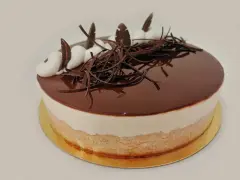 Gâteau rond avec glaçage au chocolat brillant, décoré de copeaux de chocolat et de touches de crème. Une délicieuse bavaroise vanille se cache sous le glaçage.