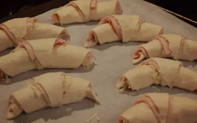 Huit croissants garnis de jambon et de fromage, prêts à être cuits. Une délicieuse pâte à pâte pour un en-cas savoureux.