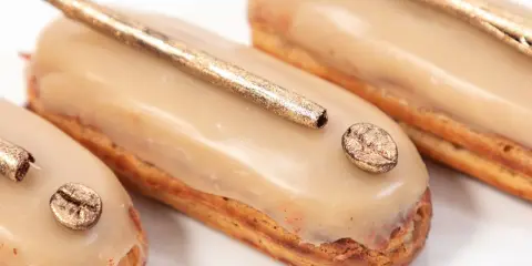 Trois éclairs gourmands, glacés à la crème patissière café, ornés d'une touche dorée et d'un grain de café scintillant.