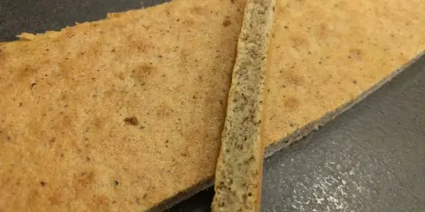 Deux fines tranches de biscuit moelleux noisette, parsemées de petits grains, reposent sur une surface sombre.