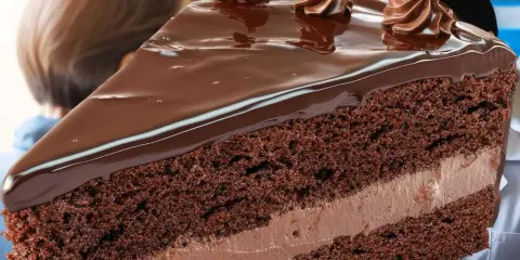 Une part généreuse de gâteau au chocolat, nappée de glaçage brillant et décorée de volutes de crème. Un délice qui rappelle l'opulence d'un opéra gateau.